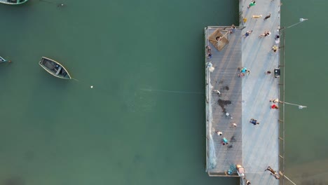 Fisherman-Throws-Out-Fishing-Net-in-the-Sea-from-Pier,-Aerial-Top-Down