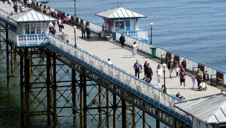 Tourist-visitors-walking-Llandudno-pier-boardwalk-sunny-landmark-attraction-on-Welsh-vacation