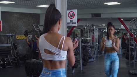 Female-bodybuilder-flexing-her-muscles-with-her-mirror-reflection-at-the-gym