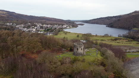 An-aerial-view-of-Dolbadarn-Castle-on-an-overcast-day,-flying-left-to-right-around-the-castle-with-slow-zoom-in-and-the-town-of-Llanberis-in-the-background,-Gwynedd,-Wales,-UK