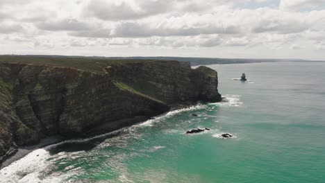 Aerial-shot-of-rugged-cliffs-along-a-coastline-with-turquoise-water-on-a-sunny-day