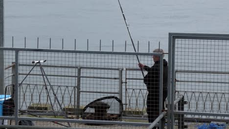 Hombre-Solitario-Pescando-Con-Caña-En-El-Puerto-Marítimo-De-Metal-Cerrado-Preparando-El-Equipo