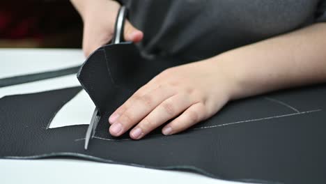 Hands-of-an-Adult-Tailor-Cutting-Piece-of-Black-Leather-with-Scissors-Close-Up