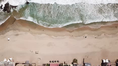 aerial-view-of-a-little-beach-town-in-Mexico,-waves-crashing-against-the-shore-people-walking