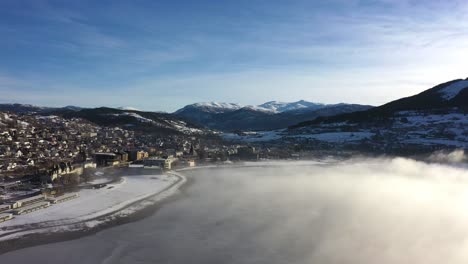 Winter-sunrise-at-Voss-Norway---Aerial-panoramic-view-of-town-with-morning-frost-haze-floating-over-Vangsvatnet-lake