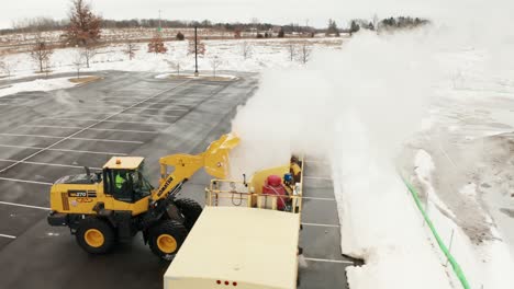 Aerial,-snow-plow-tractor-dumping-bucket-full-of-snow-into-snow-melter-machine