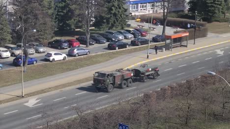 Military-trailer-truck-driving-on-Rzeszow-streets,-passing-a-group-of-kids-on-sidewalk
