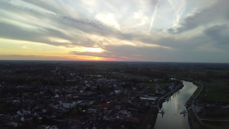 A-drone-tilts-down-over-a-city-near-the-river-Schelde-at-sunset