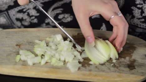 Woman-use-a-kitchen-knife-to-chop-the-onions-on-a-cutting-board,-close-up