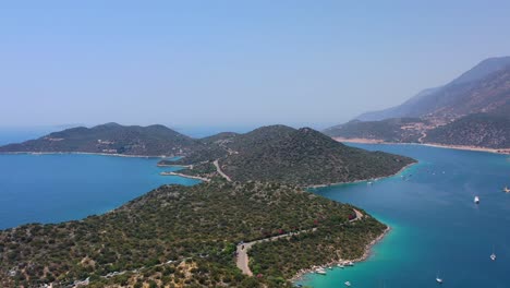 Aerial-drone-panning-left-across-a-peninsula-full-of-large-green-hills-in-Kas-Turkey-and-anchored-boats-in-the-blue-tropical-sea-of-the-Mediterranean-on-a-sunny-summer-day
