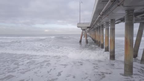 Flying-under-Venice-Pier-out-to-the-side-over-the-ocean-to-see-surfers-in-the-water