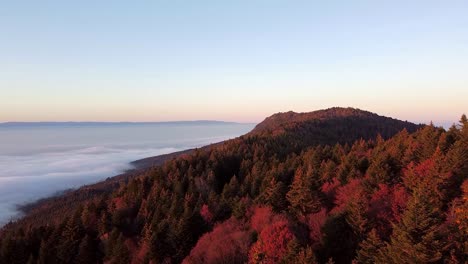 Drone-shot-of-a-Mountain-covered-in-an-Autumn-Forest-overlooking-a-Sea-of-Clouds-at-Dusk