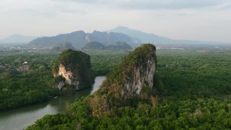 aerial-drone-panning-shot-of-large-green-limestone-mountain-rocks-with-a-mangrove-river-running-between-them-on-a-sunset-afternoon-in-Krabi-Town-Thailand