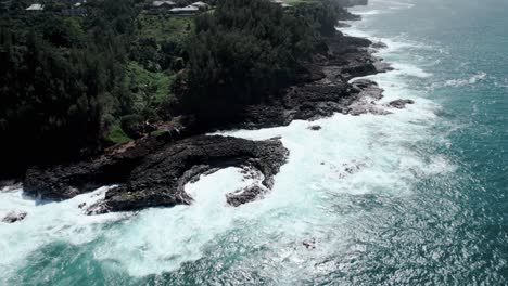 Revealing-waves-crashing-on-jagged-rocks,-Queen's-Bath,-Kauai,-Hawaii,-aerial-orbit-and-pull-back
