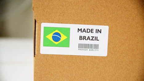 Hands-applying-MADE-IN-BRAZIL-flag-label-on-a-shipping-cardboard-box-with-products