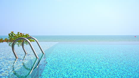 Empty-entrance-to-infinity-pool-with-metal-handrails-and-sea-on-background-on-cloudless-sky-day