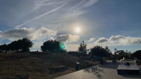 blue-sky-sun-and-clouds-moving-time-lapse-with-some-trees-fanned-by-the-wind-and-some-skaters-riding