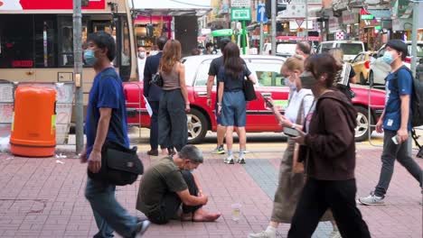 Eine-Frau-Steckt-Geld-In-Den-Becher-Eines-Bettlers,-Während-Fußgänger-Auf-Der-Straße-Von-Hongkong-Vorbeigehen