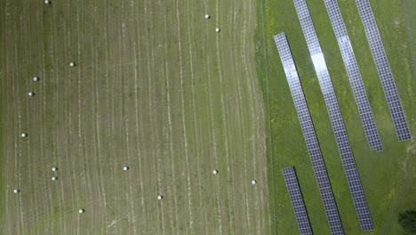 Flying-Directly-Above-Rows-of-Solar-panels-and-fields-after-harvesting-crops-with-sunlight-reflection-in-panel-cells