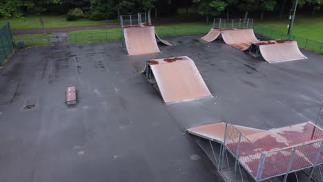 Aerial-view-flying-above-fenced-skate-scooter-park-ramp-in-empty-closed-playground