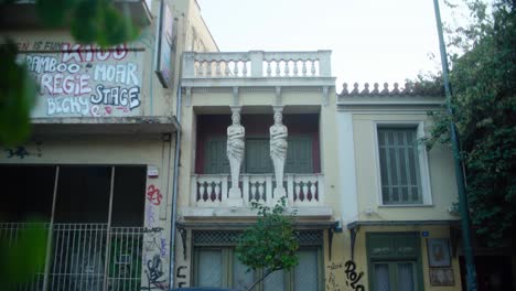 Dos-Estatuas-En-Un-Balcón-Rodeado-De-Graffiti-En-Las-Paredes-En-Atenas,-Grecia