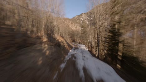 fpv-drone-flying-along-a-forest-road-up-to-the-austrian-mountains-with-a-frozen-waterfall-at-sunset