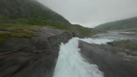 Drohnenpilot-Fliegt-Unter-Einer-Brücke-über-Einem-Wasserstrom,-Der-In-Norwegen-Bergab-Stürzt