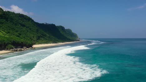 beautiful-turquoise-ocean-waves-on-Bali-coastline-in-Uluwatu-on-sunny-day,-aerial