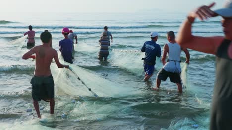 Static-shot-of-group-of-fishermen-pulling-in-fishing-net-onto-the-sea-shore-during-evening-time-in-Da-Nang-city,-Vietnam