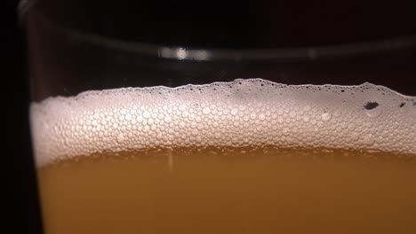 Close-up-detail:-Bubbles-fizz-and-pop-on-head-of-lager-beer-glass