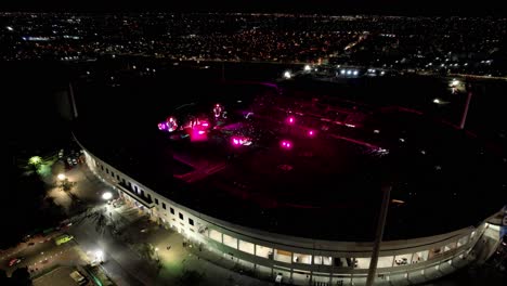 Aerial-view-of-an-illuminated-live-concert-in-stadium-in-middle-of-a-city-at-night