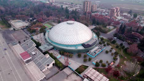 Aerial-video-of-the-Movistar-Arena-semi-spherical-dome-of-a-closed-stadium-in-the-middle-of-Santiago,-Chile
