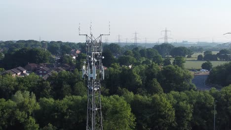 5G-broadcasting-tower-antenna-in-British-countryside-with-vehicles-travelling-on-highway-background-aerial-push-in-left-view