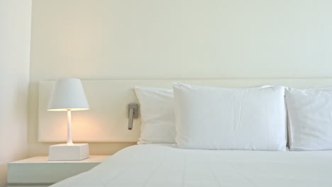 Tilt-down-on-a-modern-hotel-room-made-in-white-colors---bed-with-a-set-of-four-pillows-and-turned-on-night-lap-landing-on-cabinet
