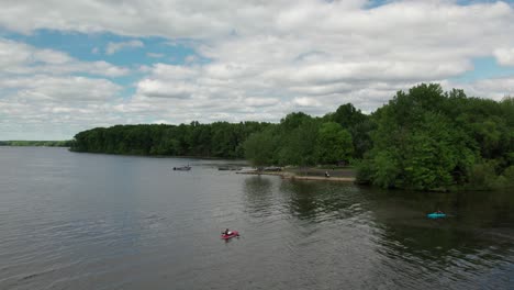 Aerial-drone-shot-of-tourists-kayaking-over-a-lake-beside-a-park-on-a-cloudy-day