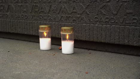 Two-white-candles-burn-at-carved-stone-war-tomb,-memorial-monument