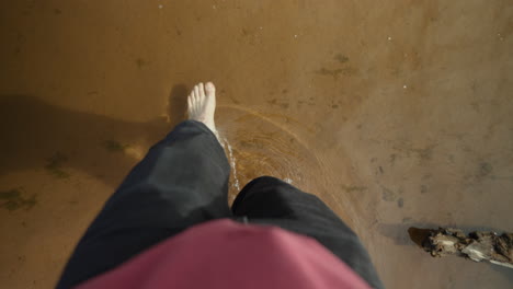 First-person-point-of-view-of-man's-bare-feet-walking-through-a-sandy-creek-to-the-other-side