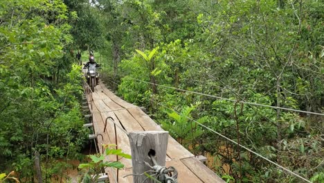 Motociclista-Cruza-Un-Puente-Colgante-Inestable-A-Través-De-La-Selva