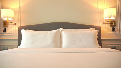 Tilt-down-shot-of-a-modern-freshly-made-resort-hotel-double-bed-with-white-blankets-and-bedsheets-and-a-set-of-four-pillows-in-a-beige-creme-white-room-interior-design