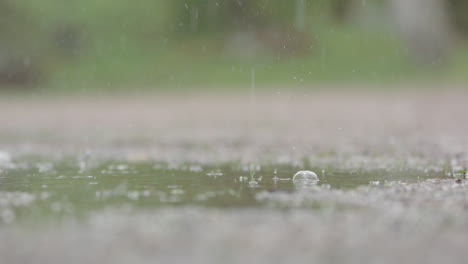 SLOW-MOTION,-CLOSEUP---Heavy-rain-droplets-falling-into-a-puddle