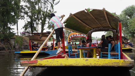 Gondolier-Using-Wooden-Rowing-Oar-To-Push-Gondola-Carrying-Tourists-Along-The-Xochimilco-Canals-Towards