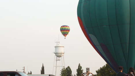 Hot-Air-Balloon-in-the-Distance-Floats-in-Clear-Sky-next-to-Water-Tower-with-Grounded-Balloon-in-the-Foreground