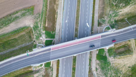 Aerial-top-down-shot-of-cars-driving-on-bridge-road-over-empty-highway-in-rural-area