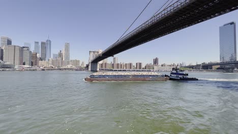 Solid-waste-management-by-barge-and-tugboat-in-New-York,-Brooklyn-Bridge
