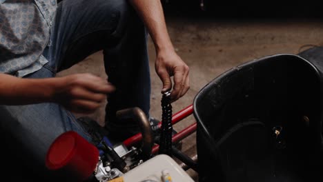 Cinematic-shot-of-mechanic-re-linking-the-chain-of-his-DIY-go-kart-with-tongs