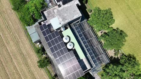 Aerial-flyover-farm-house-with-solar-panels-beside-agricultural-field-in-summer