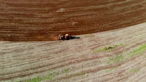 Aerial-view-shot-of-a-farmer-in-tractor-seeding,-sowing-agricultural-crops-at-field