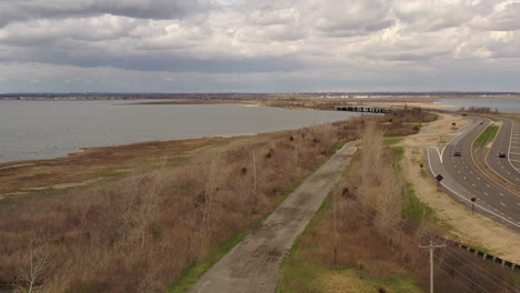 An-aerial-drone-view-on-a-cloudy-day,-over-a-dirt-road-which-is-near-a-bay