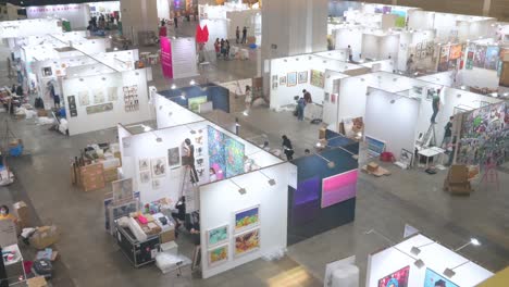 View-from-above-of-art-exhibitors-preparing-ahead-for-the-opening-of-a-contemporary-art-fair-as-they-setup-and-decorate-the-booths-and-hang-the-painting-for-sale-during-the-installation-day
