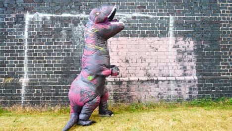 Funny-prehistoric-dinosaur-costume-stopping-and-looking-up-alongside-brick-wall